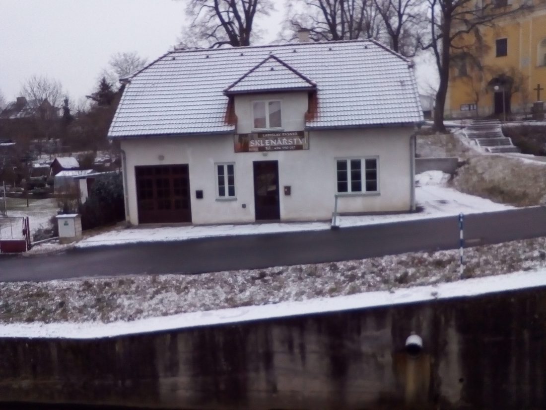 Bílý dům s cedulí Sklenářství, zasněžená střecha a ulice před ním
